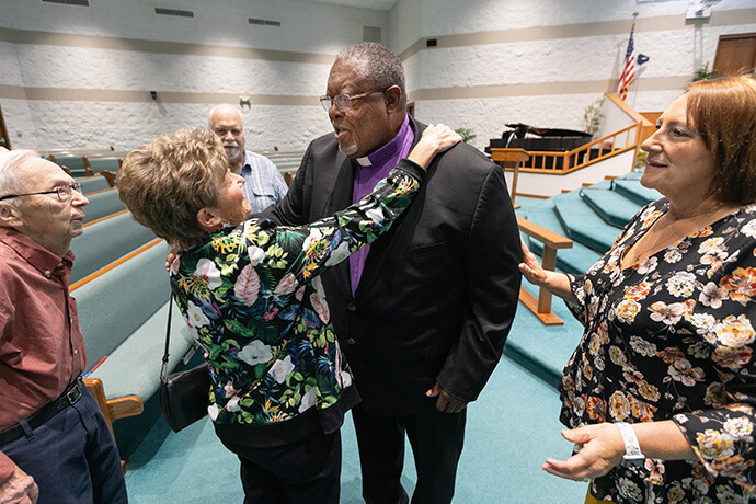 Bishop Frank Beard is greeted by Rena Humerickhouse, his former home economics teacher, and her husband, Gerald, during Beard’s return to Elkhart Faith United Methodist Church. Beard helped the church get off the ground when it formed in 1995 out of a merger of four congregations. Photo by Mike DuBose, UM News.