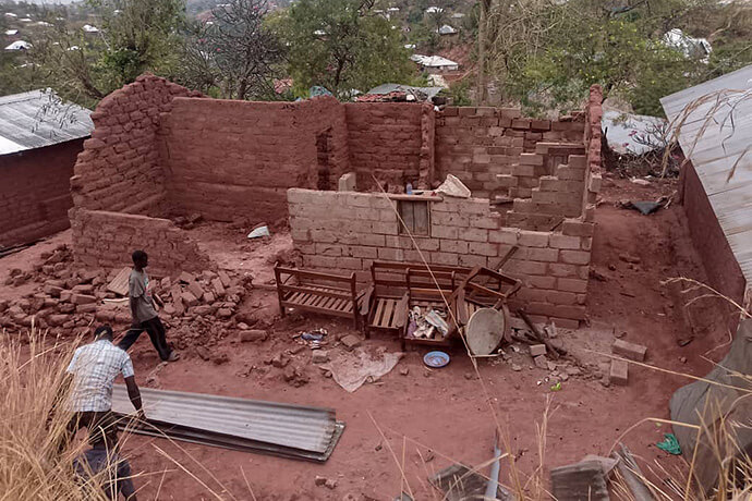 Deux hommes inspectent les ruines d'une maison de briques de terre, dont les murs se sont effondrés, laissant des débris éparpillés sur le sol rouge. Les inondations à Kalemie ont détruit 55 maisons et en ont endommagé 317 autres, forçant de nombreuses familles méthodistes unies à se retrouver sans abri. Photo avec l’aimable autorisation du Bureau de Gestion des Catastrophes de la Région Épiscopale du Tanganyika.