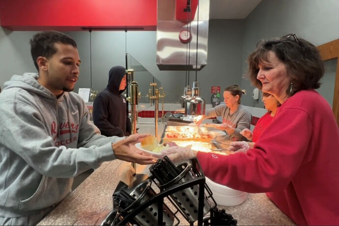 Karen Ririe hands a plate to a student during a Thanksgiving Day meal at Coffeyville Community College in Kansas. Ririe is the international student coordinator at the college. She also is a member of Oak Park United Methodist Church in Bartlesville, Okla. Video image by Lilla Marigza, UM News.
