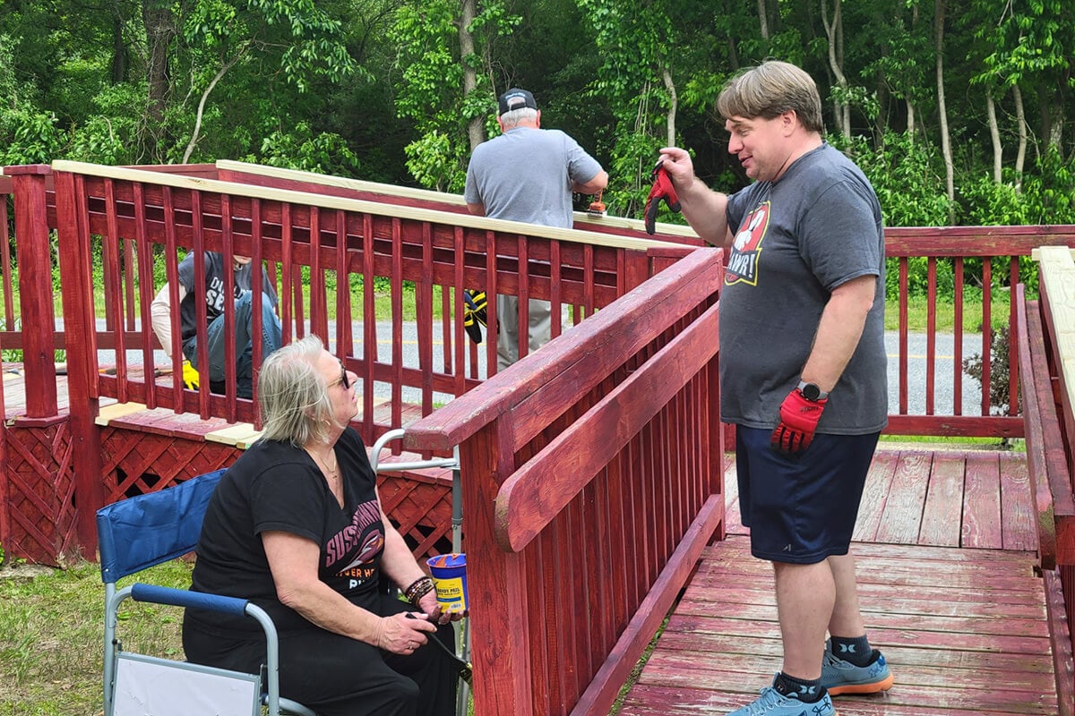 Lisa Bowser (left), lay leader of Marshallton United Methodist Church in West Chester, Pa., speaks with Christian Boehnke as church members Neal Bowser and Jonah Eckert work in the background to renovate a disability access ramp at St. John United Methodist Church in Bridgeton, N.J. St. John is the fifth-oldest historically Native American church in the denomination. The two congregations have been sharing in ministry and fellowship since 2024 as part of Marshallton’s efforts to address racial injustice toward Indigenous people its area. Photo by David Eckert.