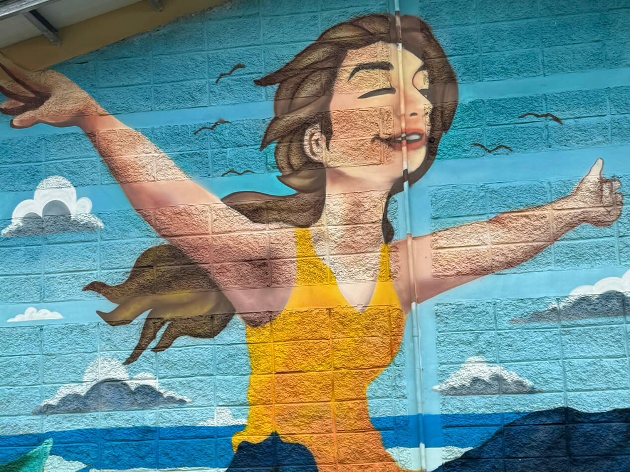 Mural que ilustra una mujer inmigrante abriendo sus brazos en símbolo de libertad y esperanza, ubicado en la fachada de uno de los edificios que albergan inmigrantes dentro del Centro de Atención al Migrante Irregular (CAMI) de Danlí, Honduras, donde funciona la clínica metodista unida auspiciada por UMCOR. Foto Rev. Gustavo Vasquez, Noticia MU.