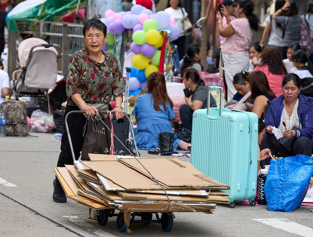 A Chinese woman pushes a cart of cardboard along Chater Road in Hong Kong on a Sunday morning. Migrant workers from the Philippines rent the cardboard for the day as they relax and visit with their friends. Sunday is the only day off for most of the women, who work as domestic servants throughout the city. Photo by Paul Jeffrey, UM News.