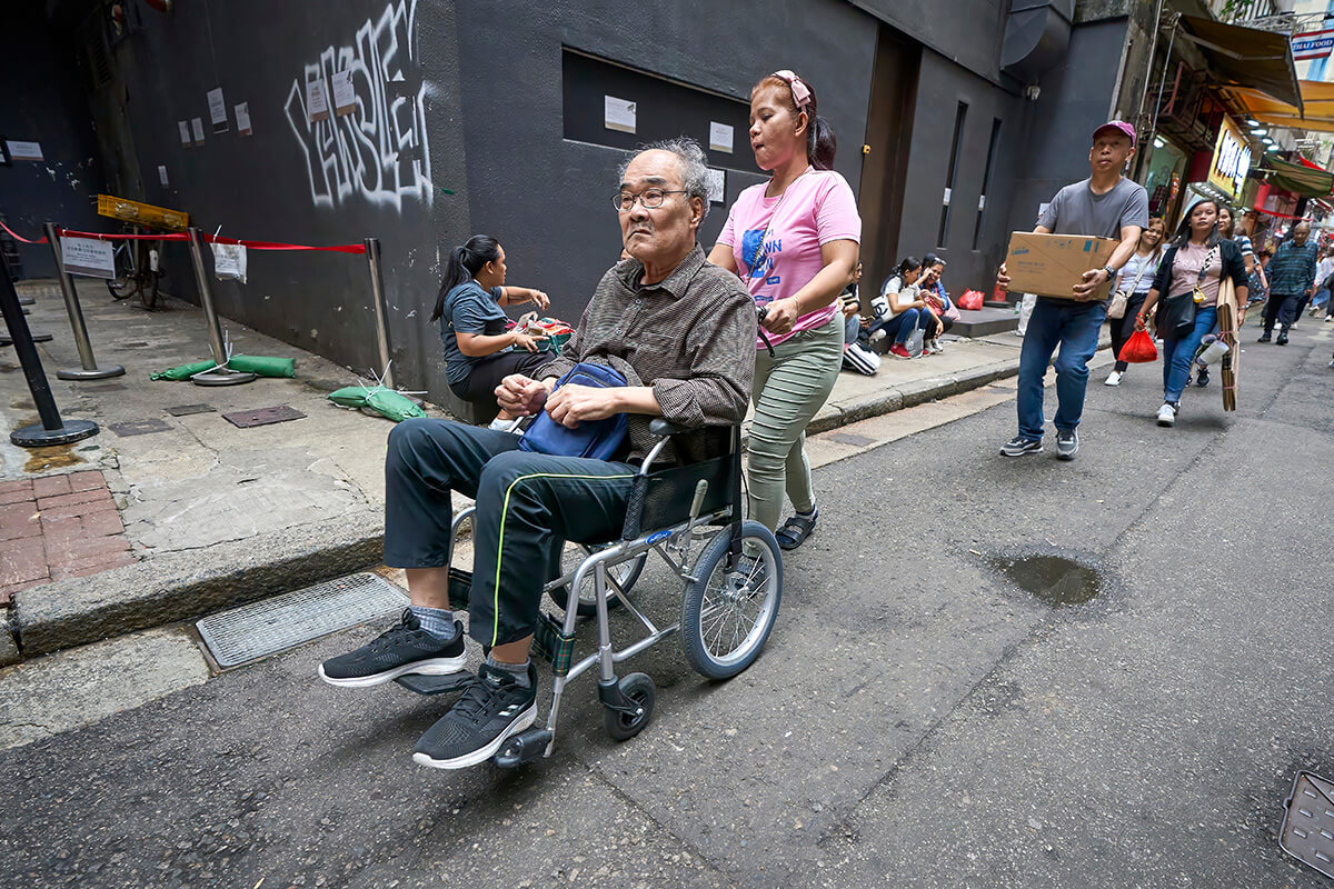 A migrant worker pushes an elderly Chinese man in a wheelchair along a street in Hong Kong. The workers, primarily from the Philippines and Indonesia, have been coming to work as domestic servants in Hong Kong for decades. Yet as city's the population grows older, they are increasingly being hired specifically as caregivers for the aged. Photo by Paul Jeffrey, UM News.