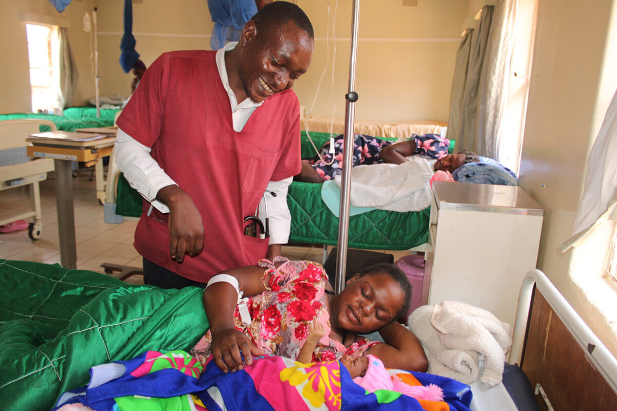 Dr. Evans Matiki smiles at Loice Mauna and her new baby while visiting patients at Old Mutare Mission Hospital in Zimbabwe. The United Methodist Church’s mission facilities at Old Mutare and Mutambara are providing improved maternity care, including daily meals for patients at the waiting mothers’ shelters. Photo by Kudzai Chingwe, UM News.