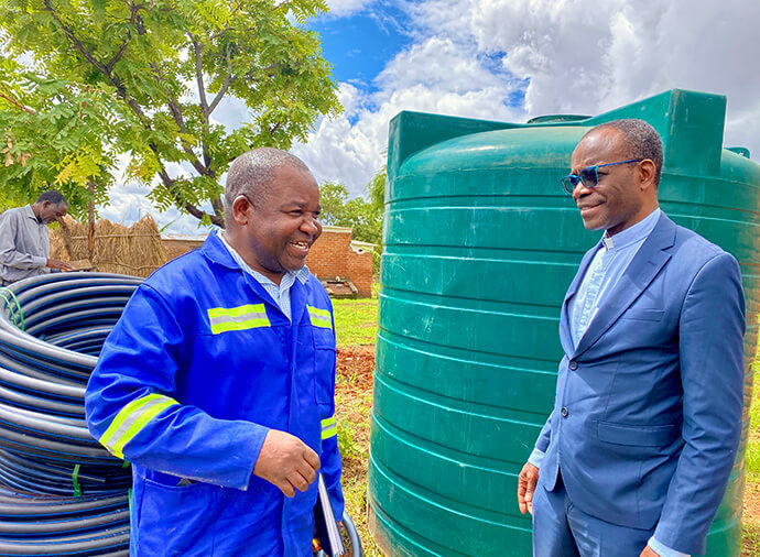Charles Namika (left), manager of Mikundi Dairy Farm in Blantyre, Malawi, speaks with the Rev. Daniel Mhone, superintendent of the Malawi Provisional Conference, beside a water container. The farm is working to incorporate a modern water system, maintaining old tanks and replacing those that are not functioning. Photo by Francis Nkhoma, UM News.