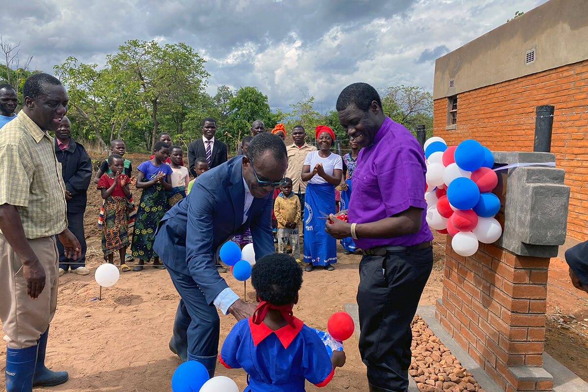 Bishop Gift K. Machinga (right) prepares to cut the ribbon at Mikundi Dairy Farm in Mikundi, Malawi, during his first visit to the country. Machinga says the church-run farm is a beacon of the income-generating projects he envisions for his episcopal area, which includes Zimbabwe, Zambia, Malawi and Botswana. He is joined by the Rev. Daniel Mhone (center), superintendent of the Malawi Provisional Conference, Kephus Mtambo (left), the farm’s project coordinator, and community members. Photo by Francis Nkhoma, UM News.
