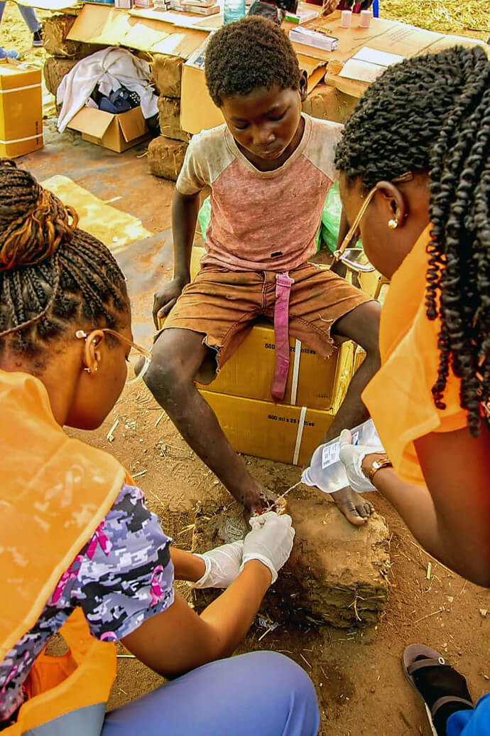 Criança recebe assistência médica. Médicos lavam a ferida contraída durante uma brincadeira para  o devido tratamento na aldeia do Mbango, durante o acampamento da OJA, em Malanje. Foto Cortesia de João Nhanga, Notícias MU.