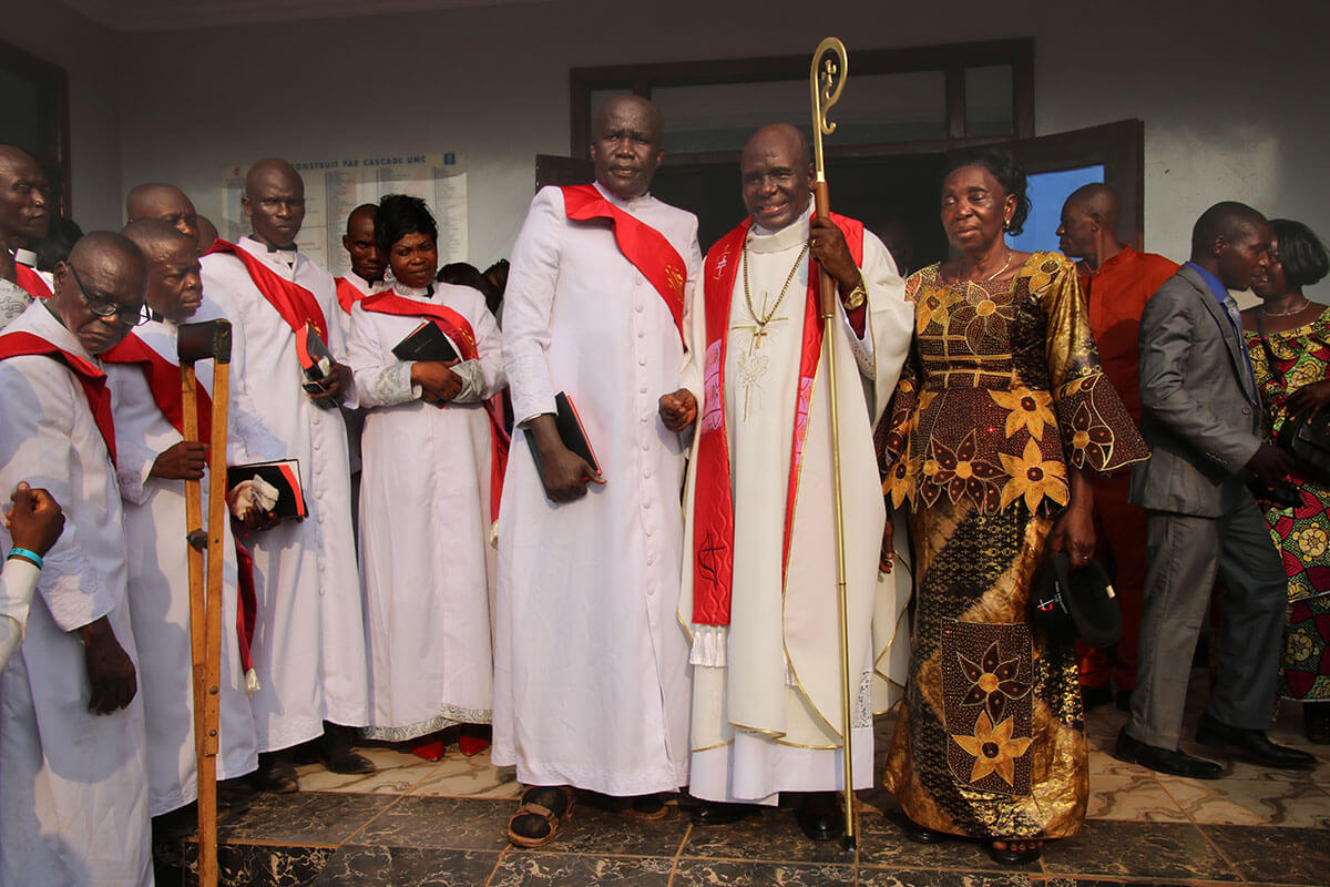 Bishop Antoine Kalema Tambwe (center) and his wife, Ngole Kitete Charlotte, greet guests in front of Bethel Cascade United Methodist Church in Bangui, Central African Republic. At left is newly ordained pastor the Rev. Christ Noël Yakizi, who serves the remote village of Cantonnier on the Cameroonian border. Photo by Chadrack Tambwe Londe, UM News.