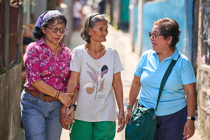United Methodist deaconesses Norma Dollaga (left) and Rubylin Litao (right) walk with Estrella Nonay in Caloocan, Philippines, in this 2024 file photo. Since her son's killing, Nonay has become an active member of Rise Up for Life and Rights, which is coordinated by Dollaga and Litao. File photo by Paul Jeffrey, UM News.