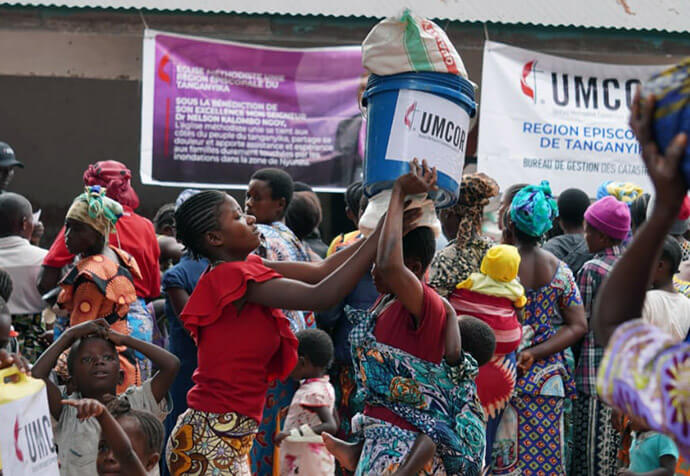 Women and children carry relief kits and humanitarian aid containers in front of the Nazareth Parish after a distribution organized by The United Methodist Church. The emergency response, supported by UMCOR, aims to stabilize people in the Tanganyika region, who are simultaneously facing the loss of their crops due to flooding and the massive influx of displaced people fleeing conflicts in North and South Kivu. Photo courtesy of the Disaster Management Office of the Tanganyika Episcopal Region.