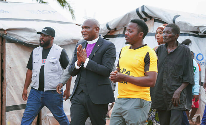 Bishop Nelson Kalombo Ngoy (center) and Richard Mushitu (left), Disaster Management coordinator for the Tanganyika Episcopal Area, walk alongside residents of a camp for displaced persons near Kalemie, Congo, to assess humanitarian needs. The pastoral visit underscores The United Methodist Church’s commitment to providing a ministry of presence and compassion to vulnerable families in these makeshift shelters. Photo by Jenovic Mandandj, UM News.