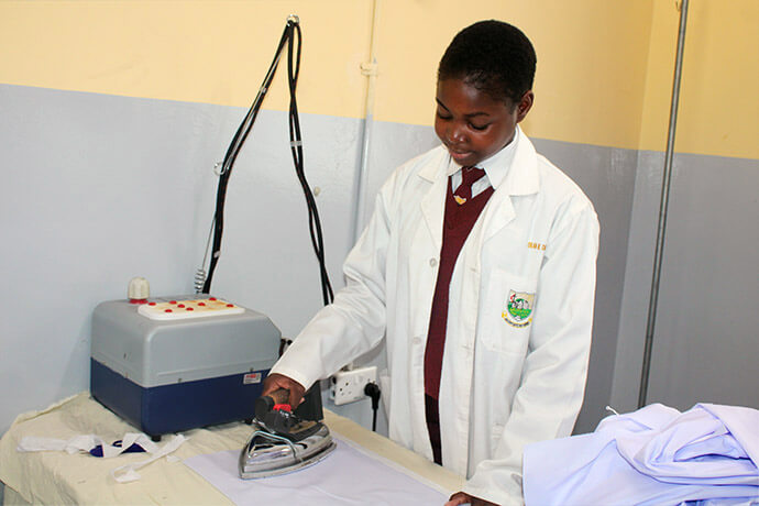 Princess Tembo uses a boiler iron to press fabric in the factory department of United Methodist Murewa High School in Murewa, Zimbabwe. The factory helps promote teacher retention and supports underprivileged students and church programs. Photo by Kudzai Chingwe, UM News.