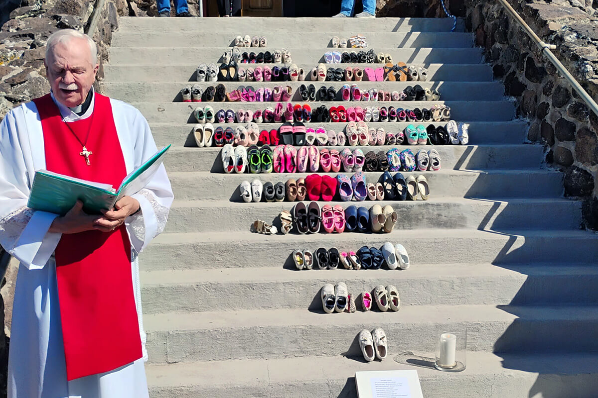 The Rev. Bob Anders (at left) leads a time of prayer on April 3, Good Friday at Cedaredge Community United Methodist Church in Cedaredge, Colo. The church displayed on its steps a memorial showing pairs of shoes to represent the 168 children and teachers killed Feb. 28 in the bombing of the girls’ school in Minab, Iran. Photos of the memorial went viral on social media. Amid the tenuous ceasefire, United Methodists continue to speak out against the war and especially threats of genocide. Photo courtesy of Anders, Cedaredge Community United Methodist Church. 