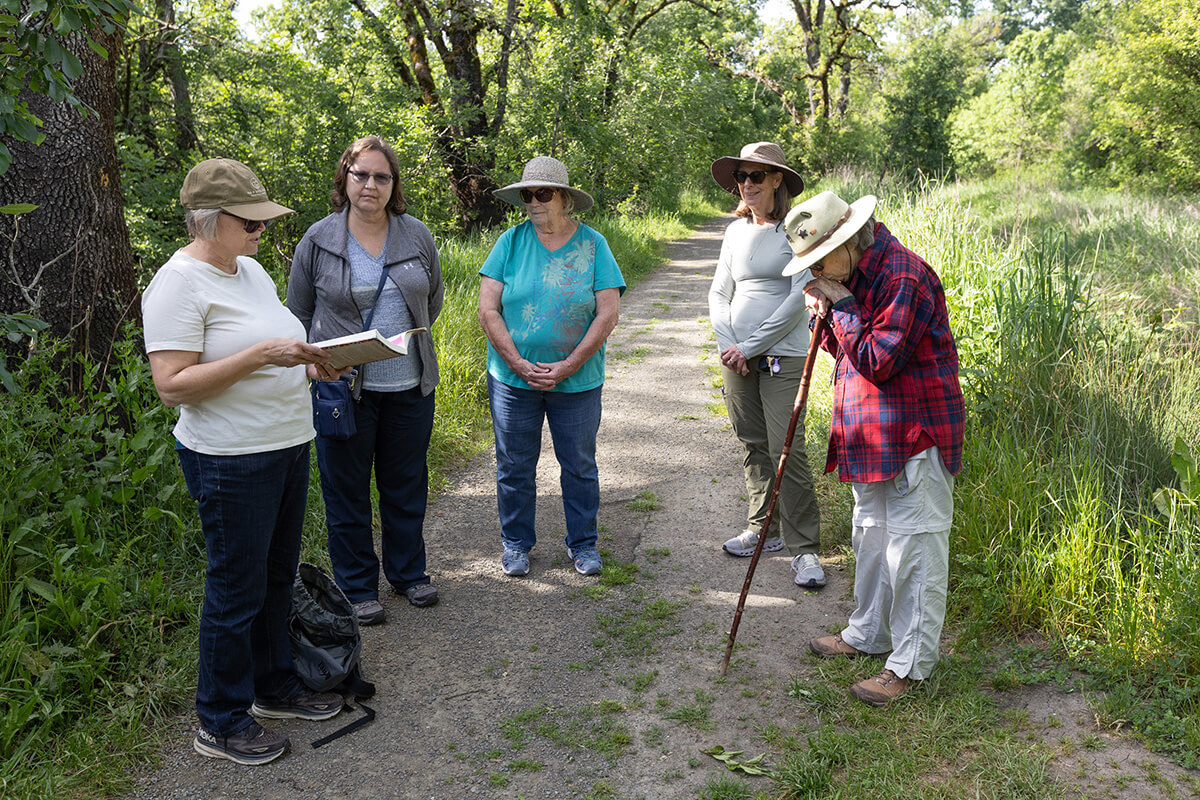 The Rev. Laurie Bayen (left) reads the Sermon on the Mount from an Indigenous version of the New Testament while standing alongside the Laguna de Santa Rosa, a 22-mile-long wetland in Sebastopol, Calif., that was once inhabited by the Southern Pomo and Coast Miwok people, during a field trip for the Sacred Ground program. Sacred Ground is a mobile outdoor walking/spirituality app developed by Bayen, a United Methodist pastor. It combines creation care and Indigenous history with calls to action. Pictured with Bayen, from left, are Cheryl LaSalle, Charlotte Fisher, Carol Wegner and Pat Schoch. 