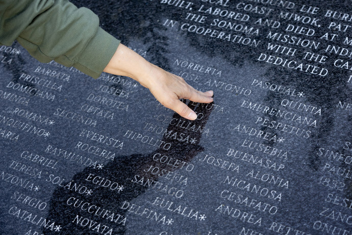 The Rev. Laurie Bayen touches one of the names at a memorial honoring some 890 Indigenous people, members of the Coast Miwok, Patwin, Wappo and Pomo tribes, who died at the Mission between 1824 and 1839. Bayen, who was leading a field trip for the Sacred Ground project, encouraged participants to choose a name that they would reflect on during the day’s hiking. Photo by Mike DuBose, UM News.