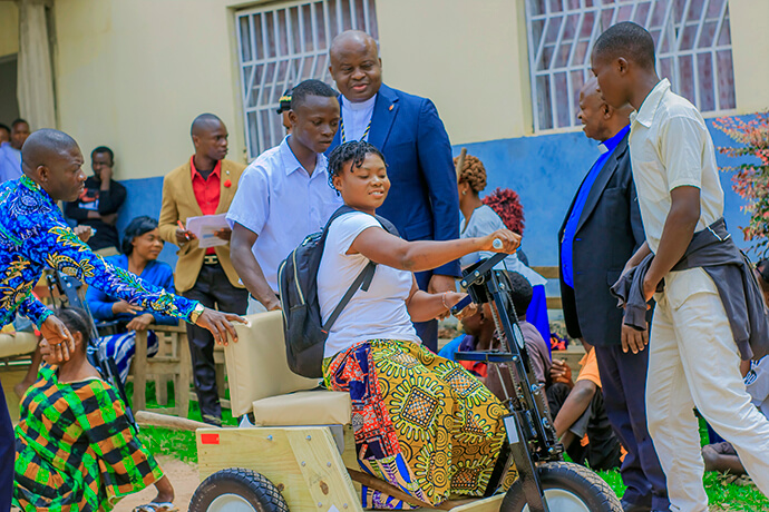 A young girl with limited mobility smiles as she maneuvers her tricycle equipped with hand cranks for the first time as Bishop Mande Muyombo (standing at center) and other church leaders look on. This project aims to promote social and educational inclusion by enabling young people and adults to travel with dignity to their places of work or study. Photo by Yamba Kisonga Barthélémy, UM News.