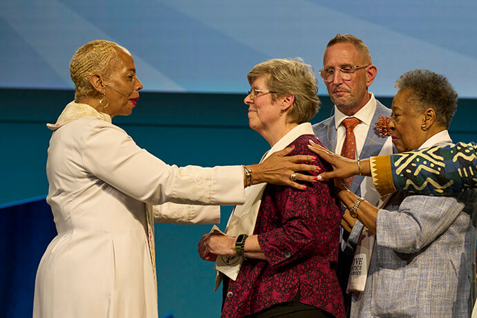 Bishop Tracy S.Malone congratulates Elizabeth Kroll after her consecration as a deaconess on May 15, 2026, at the United Women in Faith Assembly in Indianapolis. Also laying on hands are Scott James-Vickery and Clara Ester. Photo by Paul Jeffrey, United Women in Faith.