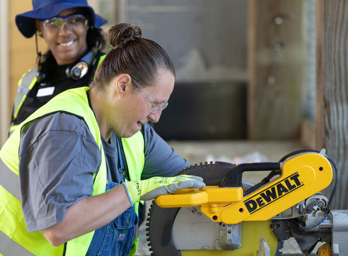 Sarah Bernardo learns to use a miter saw at the Women in Construction program in Biloxi, Miss. Watching her is instructor Ethel Williams-Haynes. 