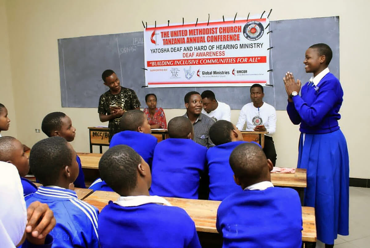 A student signs for her classmates as Michael Pius (standing in black shirt), a United Methodist health officer, provides information to Deaf students at Buhongwa Secondary School in Mwanza, Tanzania, in 2021. Part of the Tanzania Conference’s Yatosha Deaf Ministry, the outreach includes spiritual guidance and teaching practical skills that empower Deaf students to live healthier and more fulfilling lives. Photo by Robert Aloyce, UM News.
