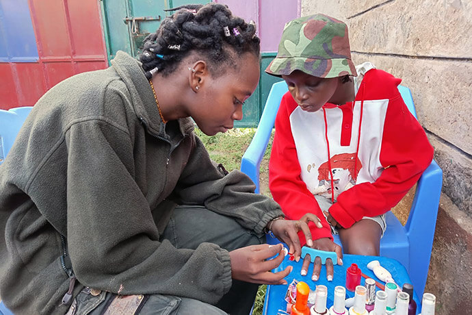 Gloria Kache (left) paints Clementina Kalunde’s nails at Parkview Kitengela United Methodist Church in Nairobi, Kenya. Kache is a beneficiary of the church’s No Girl No Cry initiative, which empowers young girls in the community through education and mentoring. She now volunteers with the church’s Mumo Educational Center. Photo by Jackline Mwende.