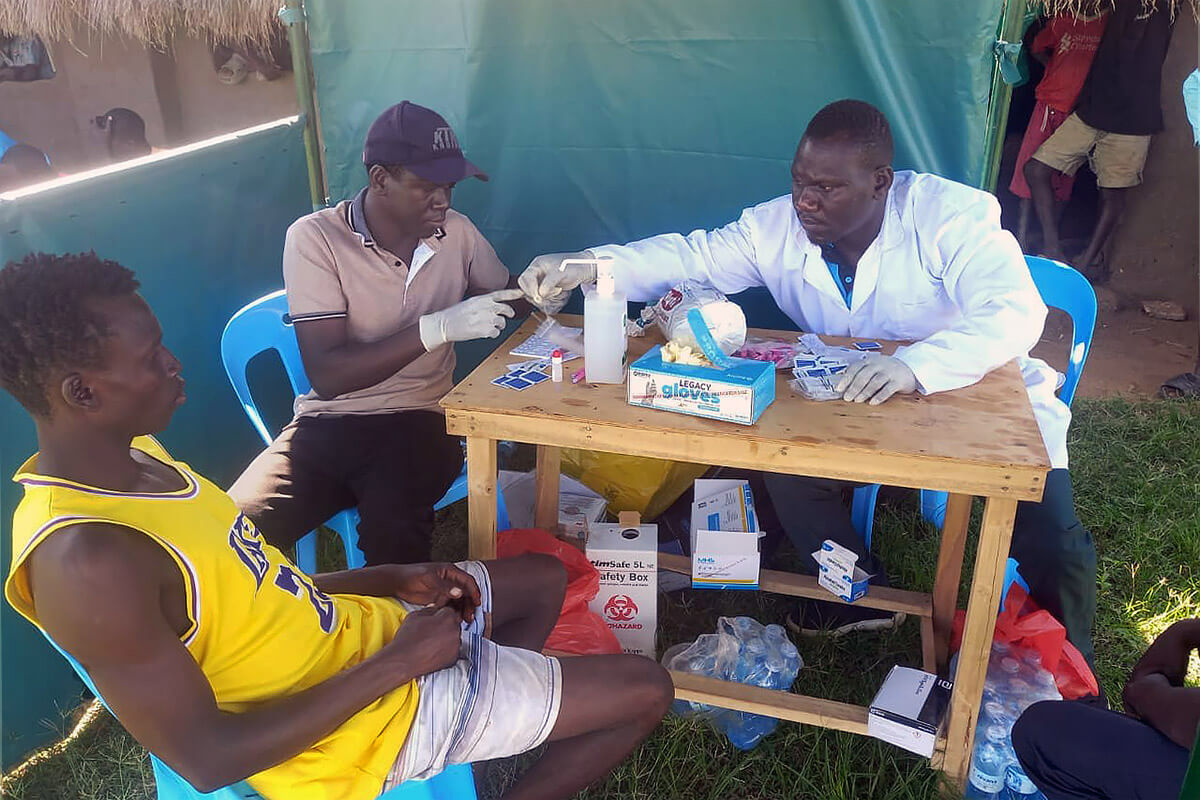 Lab technician Arike Joel (right) conducts HIV testing during a soccer tournament hosted by The United Methodist Church at Imvepi Settlement in Arua, Uganda. The medical testing is part of the church’s Kick Out HIV campaign, which focuses on HIV prevention and self-care in refugee camps. While players battled for victory on the pitch, health workers offered confidential HIV testing and counseling on the sidelines. Photo by Juma Denis Daniel, UM News.