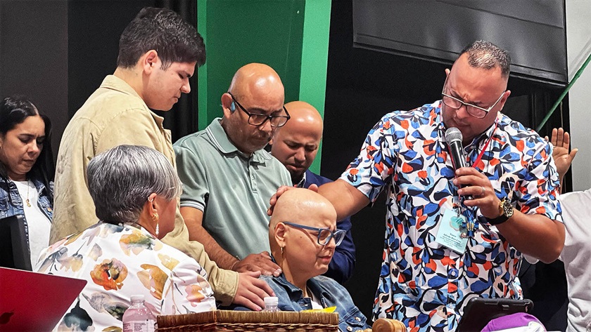 Después de presentar su informe ante la plenaria, familiares y líderes de la iglesia elevan una oración por la salud de Vilmarie Rivera Sierra, Directora Ejecutiva del programa Rehaciendo Comunidades con Esperanza (ReHACE) y del Centro de Intercesoría y de Servicios Integrales para la Mujer (CDIM) de la Iglesia Metodista de Puerto Rico. Foto Rev. Gustavo Vásquez, Noticias MU.