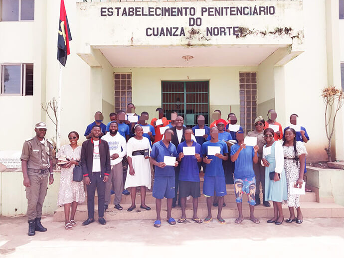 Alguns reclusos e membros da Igreja alinhados a frente do  edificio penitenciário onde os reclusos  demonstram os seus certificados de baptismo. Foto cortesia  da comissão de comunicação da Igreja Central de Ndalatando, Angola. Notícias MU.