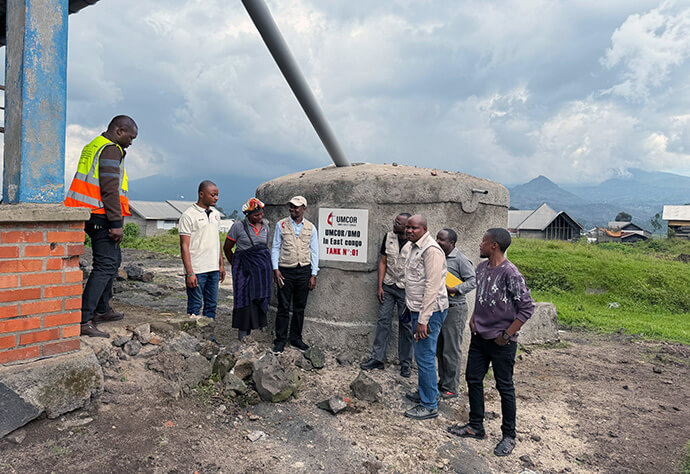Jean Tshomba (in hat), Dr. Damas Lushima (to the right of sign) and members of a humanitarian team inspect a water tank funded by UMCOR in the village of Kibumba, 17 kilometers north of Goma, Congo. The tanks are connected to rooftops to capture water during the rainy season and store it for later use, reducing the incidence of water-related diseases. Photo by Jolie Shabani, UM News.
