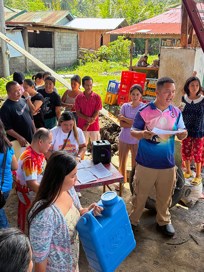 Marife Cambel (seated at center), a United Methodist Young Adult Fellowship leader, helps distribute relief supplies in the Tango barangay in Glan, Philippines, during a relief operation led by General Santos United Methodist Church on July 25. More than 200 families received supplies and other support. Photo courtesy of Marife Cambel. 