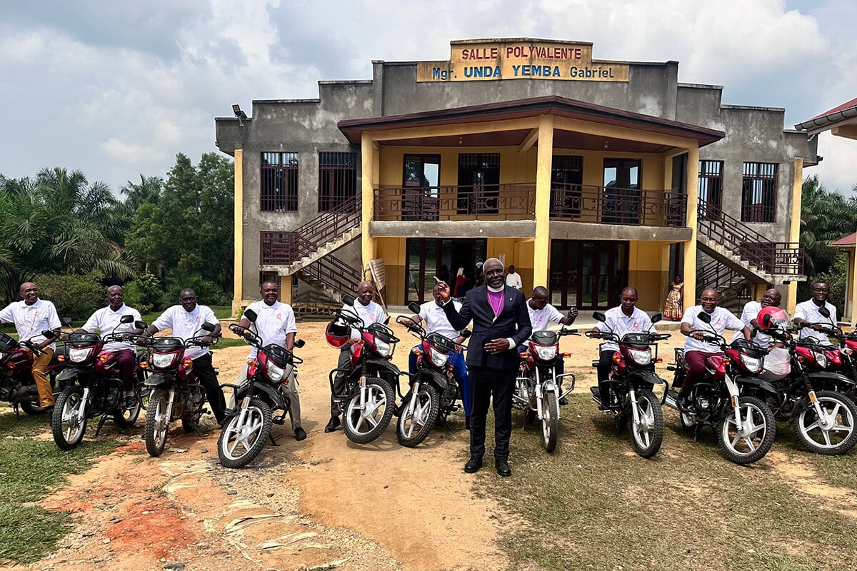 Bishop Antoine Tambwe Kalema (center) poses for a photo with the 11 district superintendents from the Eastern Congo Conference who received new motorcycles as a gift from the bishop during the 2026 annual conference. Many of the church leaders had spent years traveling on foot or by bicycle to minister to their communities. Behind them is the Mgr. Gabriel Unda Yemba Multipurpose Hall at the Mama Lynn Center in Kindu, Congo. Photo by Chadrack Tambwe Londe, UM News.