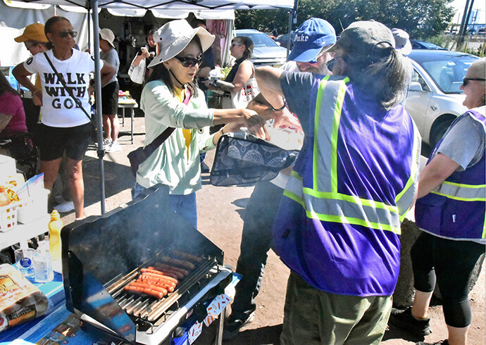 The Rev. Dianne McGraff (left, in “Walk With God” T-shirt), pastor of Community United Methodist Church of Hoboken, N.J., watches as volunteers prepare to serve grilled hot dogs to “Prayerful Witness” attendees and visitors to the Delaney Hall detention center on Aug. 15. Photo by John W. Coleman, UM News. 