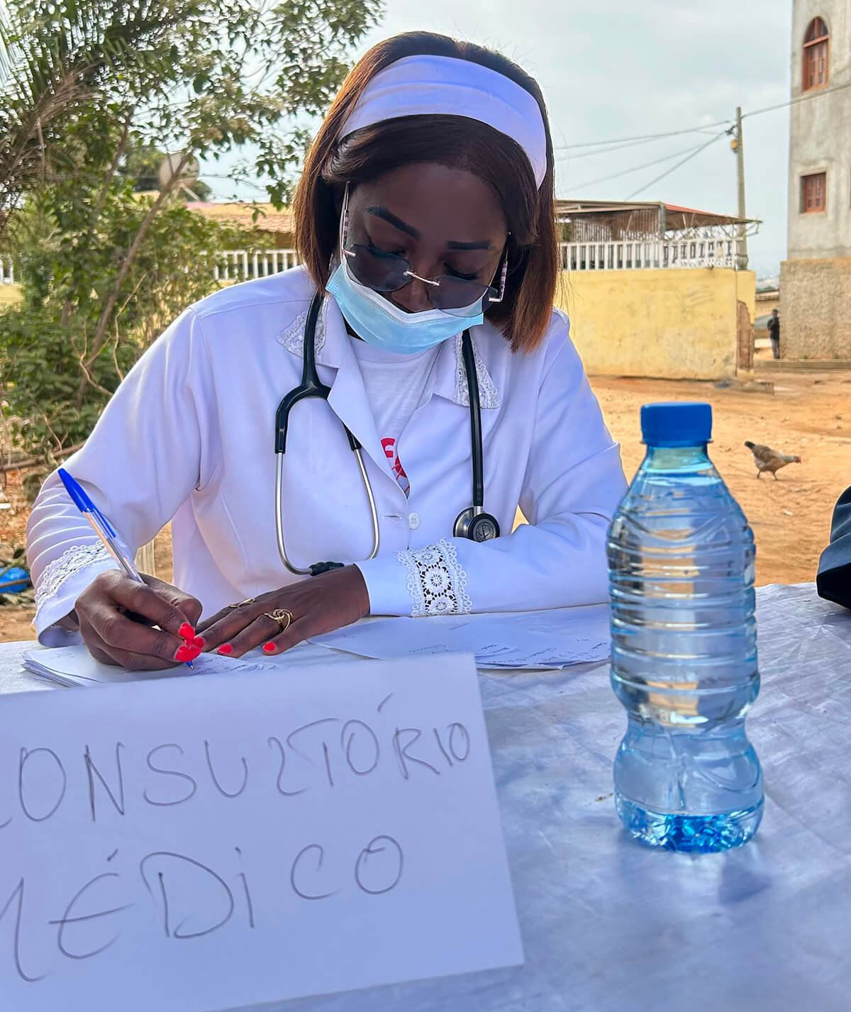 Dra. Rosa Manuel, num consultório médico improvisado no quintal da Igreja Metodista Unida de Luis Correia Kizembe em Luanda fazendo a prescrição médica de uma paciente no seu programa social de assistência médica e medicamentosa. Foto cortesia de Orlando da Cruz, Notícias MU.