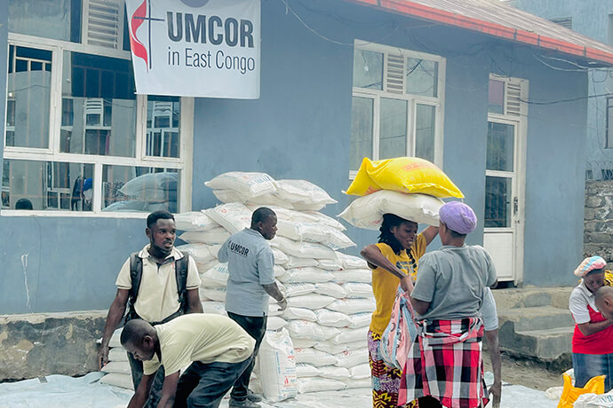 Une femme charge des sacs de farine sur sa tête avec l’aide de bénévoles méthodistes unis lors d’une remise de rations alimentaires à Goma, au Congo. En plus de soutenir les 300 familles ciblées, le programme de l’UMCOR a également fourni des kits alimentaires à l’orphelinat méthodiste uni de Goma. Photo : Jolie Shabani Mulebinge, UM News.