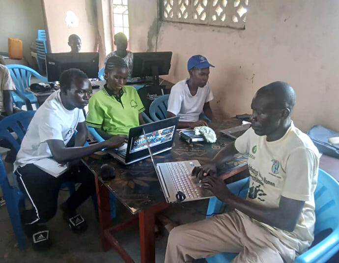 The Rev. Faustino Duku (center in white shirt), dean of district superintendents for the South Sudan United Methodist Church, delivers remarks during the presentation of computers and other equipment in the Ariaze community in Uganda’s Rhino Camp Settlement on Aug. 18. Duku said he expects the Youth Digital Literacy Project to benefit the church, youths and the community at large. Photo by Mudomo Joseph, UM News. 