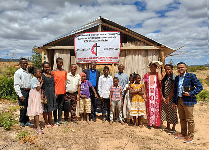The Rev. Eric Kalumba Nkulu (center in blue shirt), a Global Ministries missionary from Congo, is surrounded by a young United Methodist congregation in Ambilobe, Madagascar. After meeting under a tree for six months, the group built a small shed on a plot of land donated by one of the faithful. Photo by Mamisoa Natacha, UM News.