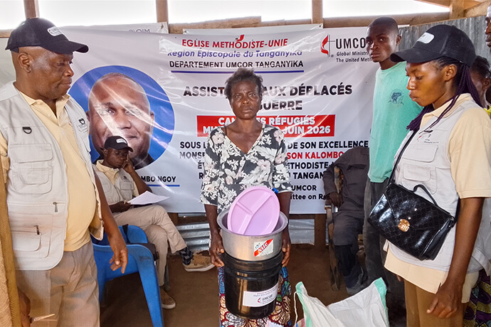 Mande Masudi Deborah, veuve et mère de cinq enfants, reçoit ses provisions lors de la distribution humanitaire organisée le 2 juillet au camp de Mushaba. Composé de farine de maïs, de riz, de haricots et d’ustensiles ménagers, le don met en pratique le ministère social de l’Église méthodiste unie auprès des familles déplacées vivant dans une extrême précarité. Photo de Mpyana Wa Kasongo M. Pascal, UM News.